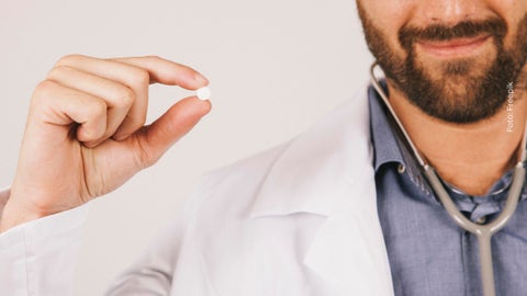 Médico sostiene una píldora en sus dedos