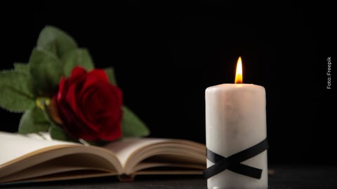 Vela blanca rodeada de una cinta de luto junto a una biblia con una rosa roja